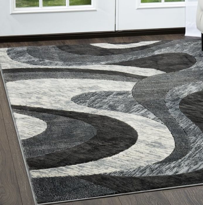 The grey and white abstract swirly-patterned rug laid out on a hardwood floor.
