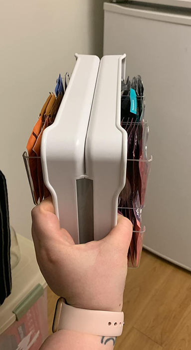 A reviewer is holding a tea stand filled with tea bags, highlighting its slim design.