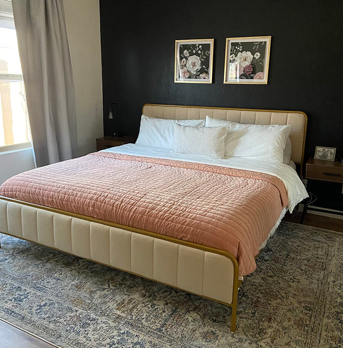 A beautifully made bed with a white duvet and a pink throw, set in a bedroom featured in a home decor shopping article