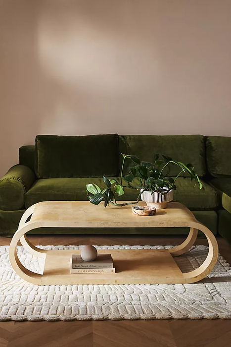 A contemporary living room featuring a uniquely curved wooden coffee table paired with a plush green sofa.