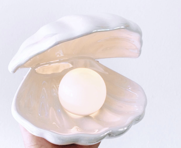 A hand gently holding the iridescent shell lamp, with the glowing pearl light shining from within.
