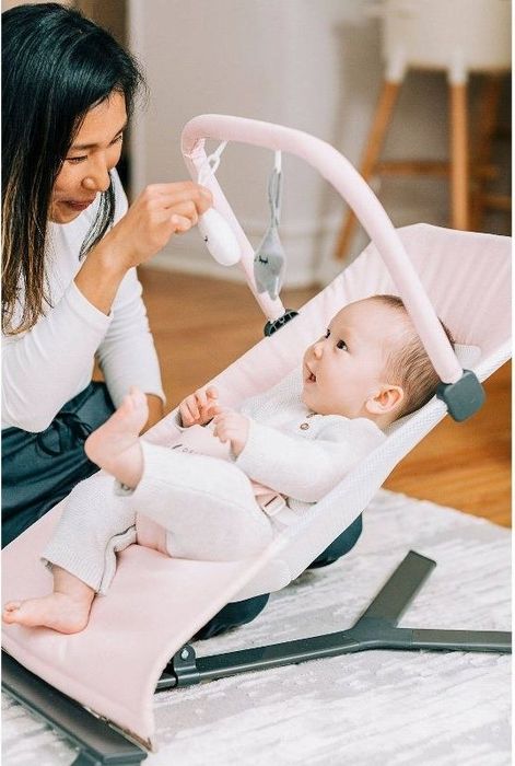 An adult interacts with a baby seated in a bouncer.