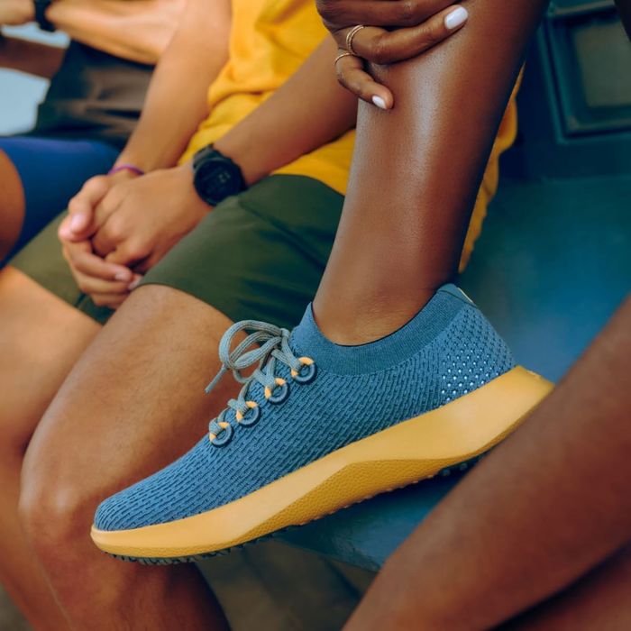A model showcasing the blue and yellow Allbirds Tree Dasher 2 sneaker.