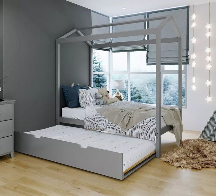 A children's bed with a canopy frame and pull-out trundle, surrounded by twinkling fairy lights and plush stuffed animals, set in a chic, modern bedroom.