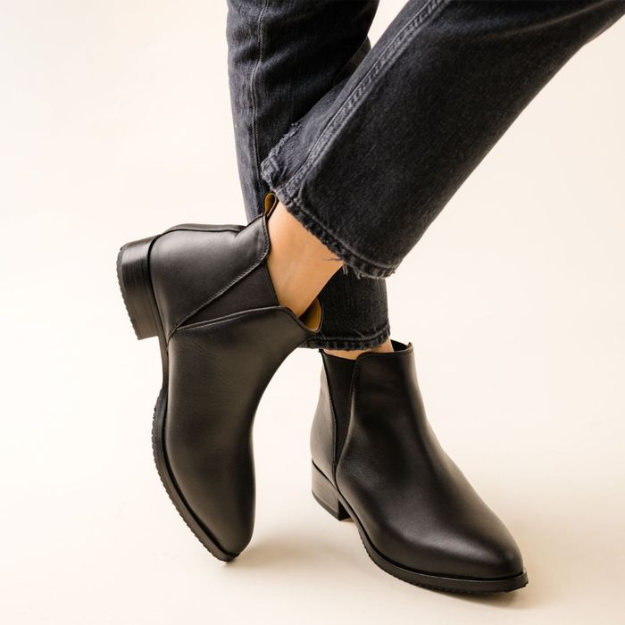 A person wearing black ankle boots paired with cuffed jeans.