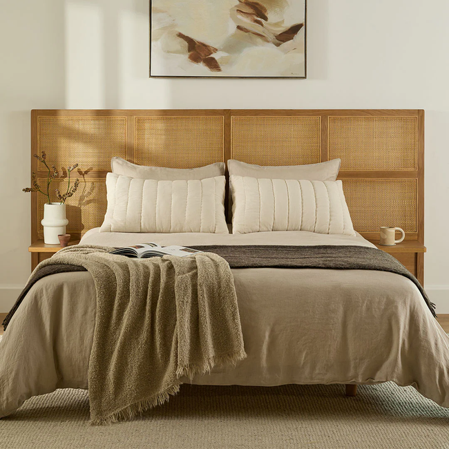 An elegantly made bed featuring neutral-toned linens and a textured throw blanket, complemented by a beautiful cane headboard.