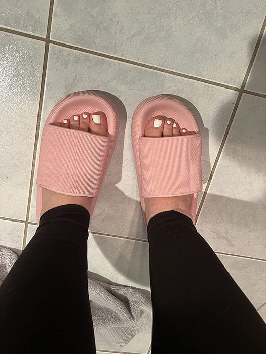 A reviewer wearing a pink pair of the same slides.
