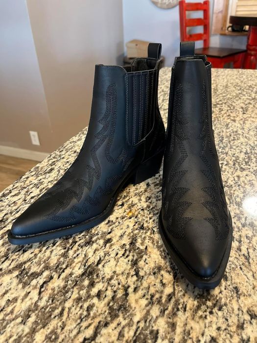 A pair of black Western-style ankle boots with intricate stitching details, placed on a kitchen counter