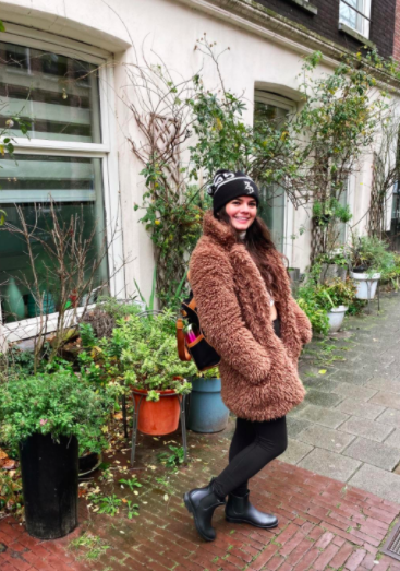 A reviewer sports black Chelsea rain boots paired with black leggings, a brown teddy coat, and a black beanie while enjoying a rainy day in Europe.