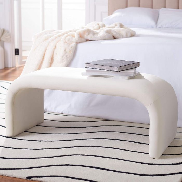 A sleek curved bench adorned with books, placed at the foot of the bed.
