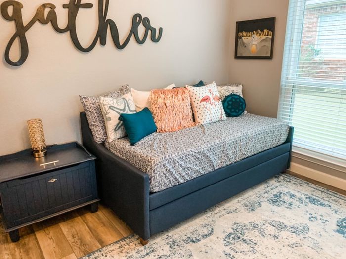 A trendy daybed featuring patterned cushions and an assortment of pillows, placed in a cozy room with 'gather' decor adorning the wall.