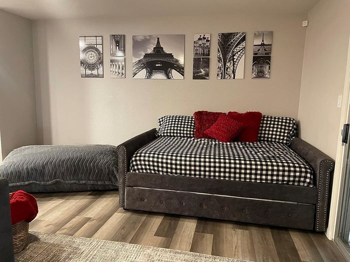 A modern living room featuring a plaid-upholstered daybed with red pillows and Paris-themed wall art that adds a chic vibe.