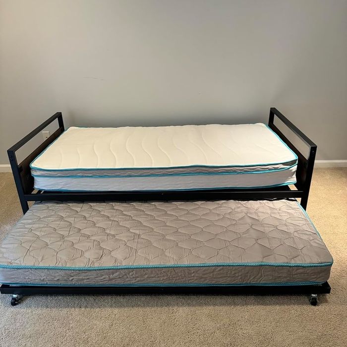 A trundle bed with one mattress on top and another neatly stored underneath, placed in a carpeted room.