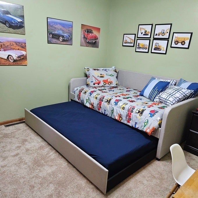 A children's bedroom featuring a car-themed daybed with a trundle and car-inspired decor adorning the walls.