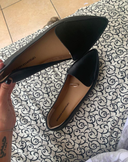 The reviewer is holding up the same shoe style in black with their hand.