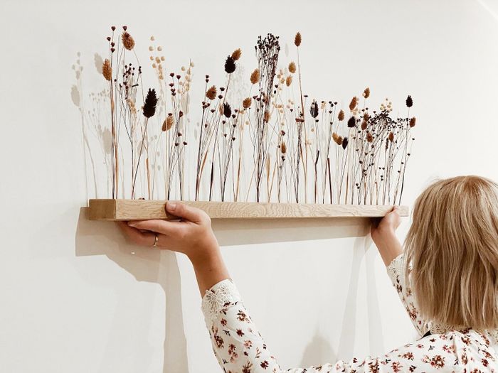 A natural wood shelf with dried flower stems carefully placed upright on top.