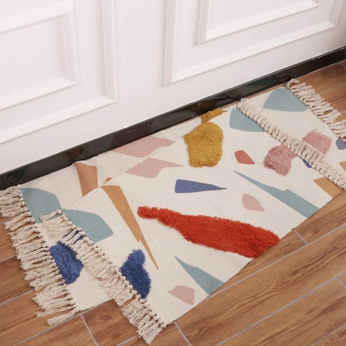 Beige tasseled rugs layered on top of each other, each featuring various materials and colorful, geometric patterns that add texture and visual interest.