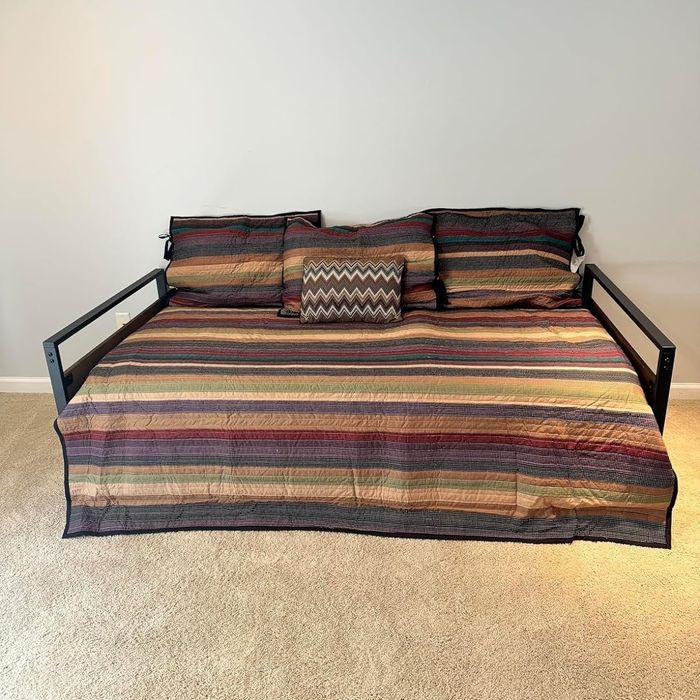 A daybed adorned with striped bedding and a decorative zigzag pillow, placed on a carpeted floor, ideal for versatile home decor.