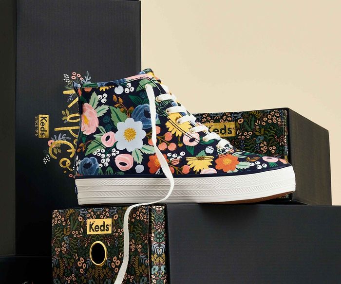A trendy floral high-top Keds shoe is showcased with branded boxes in the background, highlighting its chic design.