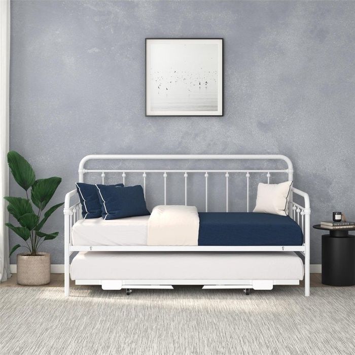 A sleek, modern metal daybed with a trundle, adorned with blue and white bedding, positioned in a minimalist room that includes a plant and framed artwork on the wall.