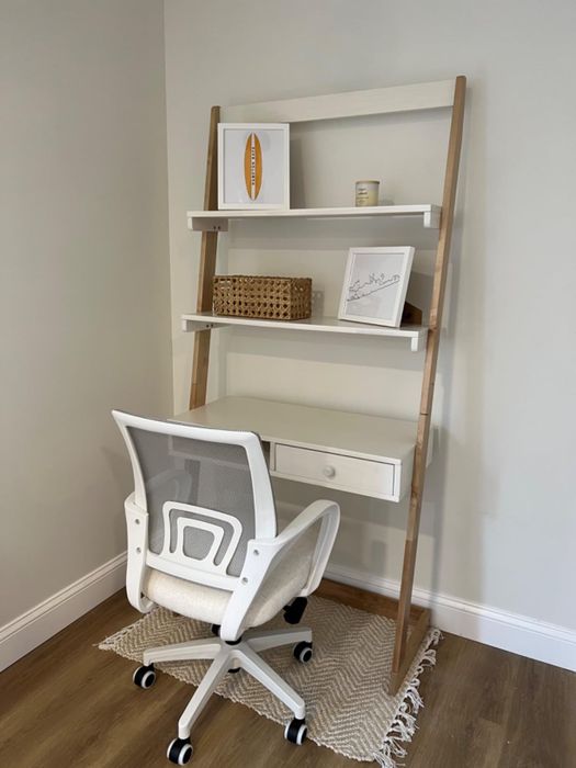 An office chair positioned in front of a leaning shelf filled with decorative pieces and a drawer