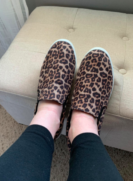 The reviewer is seen wearing brown leopard-print slip-on sneakers alongside black leggings.