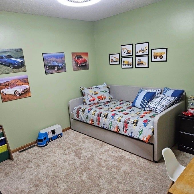 A kids' room with car-themed wall art and bedding, toy trucks scattered on the floor, and a gray bed as the centerpiece.