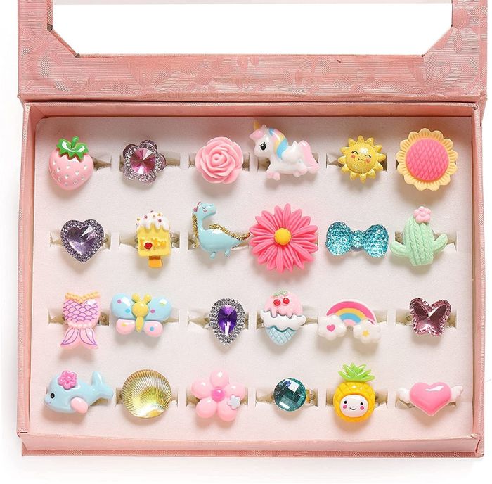 A pink box filled with 24 rings in cute designs like dinosaurs, strawberries, bows, cacti, pineapples, and more