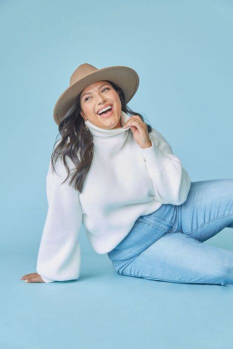 The model is seen wearing a white sweater with wide, flowing sleeves.