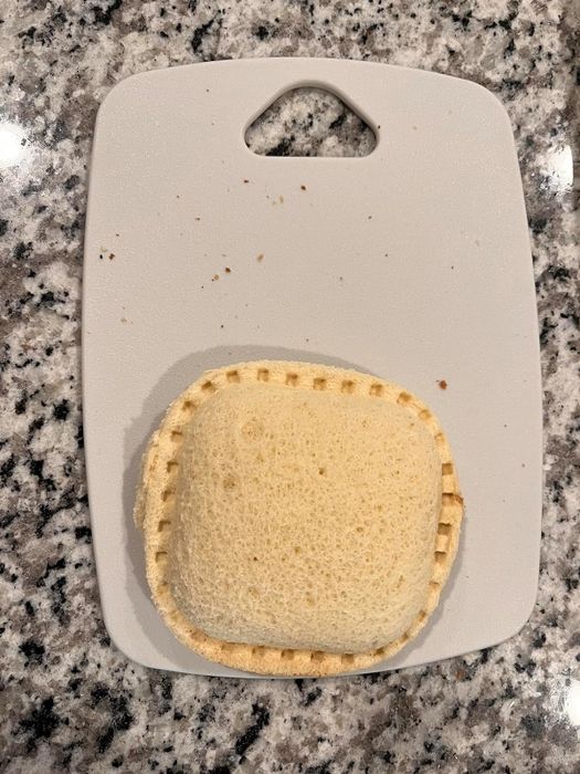A reviewer's image of a neatly sealed square sandwich positioned on a white cutting board atop a granite countertop