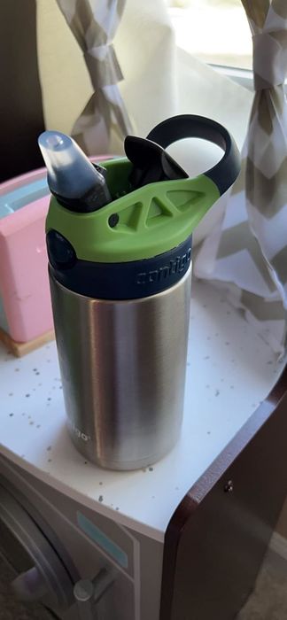 A reviewer’s photo of a stainless steel Contigo water bottle with a green and black spout, placed on a speckled countertop