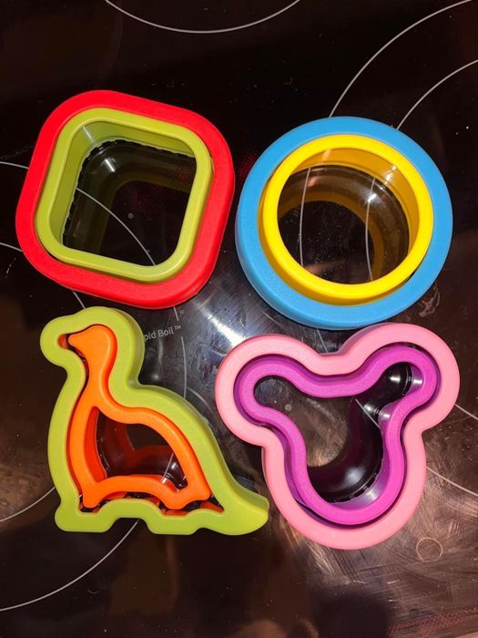 A reviewer's snapshot showcasing sandwich cutters shaped as squares, circles, dinosaurs, and bear faces, displayed on a stovetop