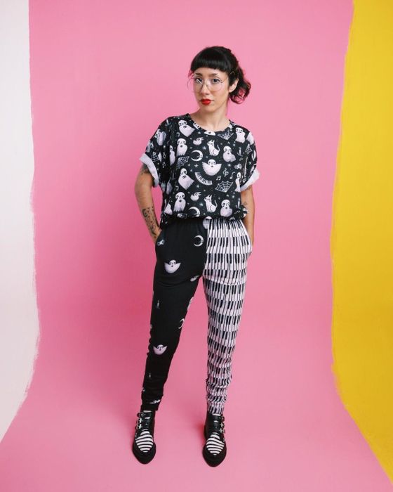 The model wears pants with a unique split design: one side features piano keys, while the other is adorned with black ghosts, moons, and bugs.