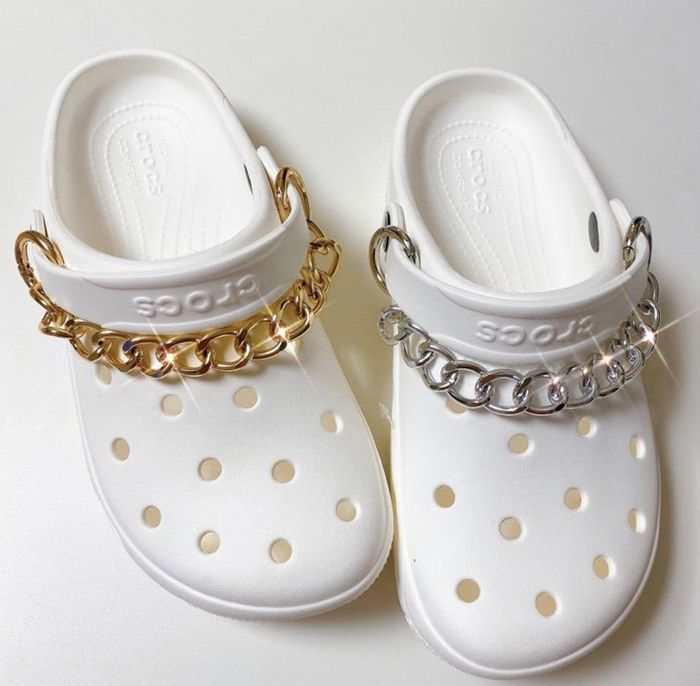 A set of white Crocs, featuring chunky chains wrapped around the tops for added flair.