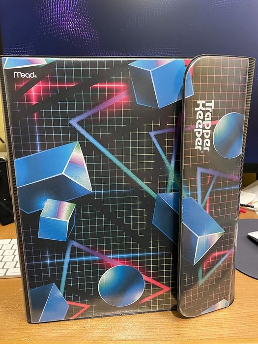 Reviewer's photo of a Trapper Keeper by Mead showcasing a geometric design binder with cubes and spheres on a grid background