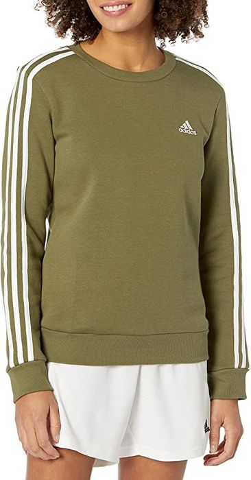 A model dons an olive green sweatshirt with three iconic Adidas stripes running down the sleeves, paired with shorts.