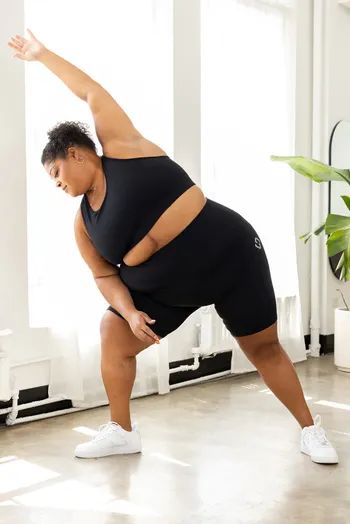 A model demonstrating a stretch while wearing a sleek black workout outfit.