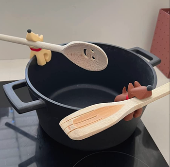 Two dog-shaped spoon rests, one beige and one brown, attached to the side of a pot holding spatulas.