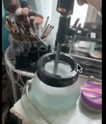 A reviewer dipping an electric vibrating makeup brush cleaner into a small pot of soapy water.