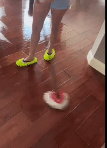 A model is using a mop to clean the floors while wearing green mop slippers on their feet.