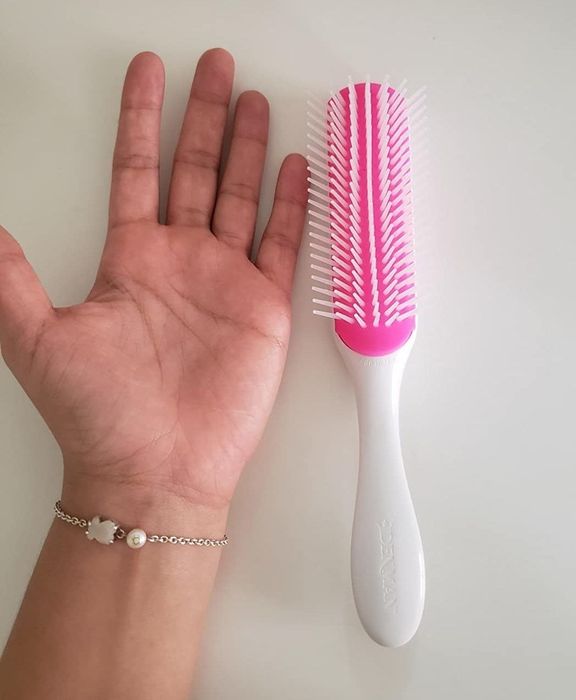 A reviewer's hand next to a white and pink Denman brush on a table