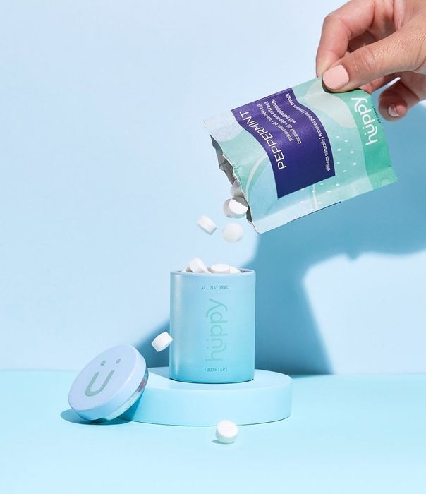 a hand pouring tablets from a pouch into a blue tin
