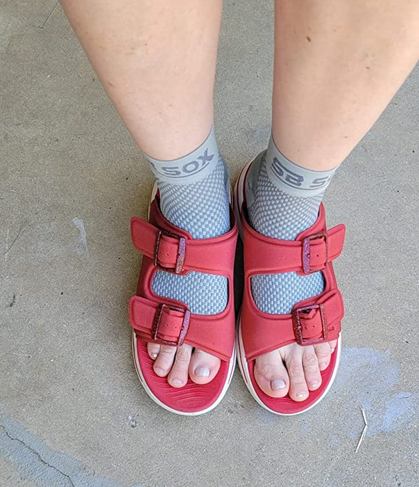 A reviewer wearing gray compression socks paired with red sandals.