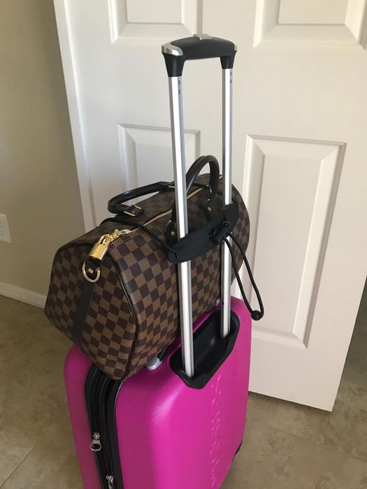 A bungee cord securing a handbag to the top of a suitcase.