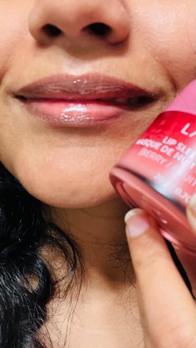 A reviewer is wearing the lip mask while holding the pink package.