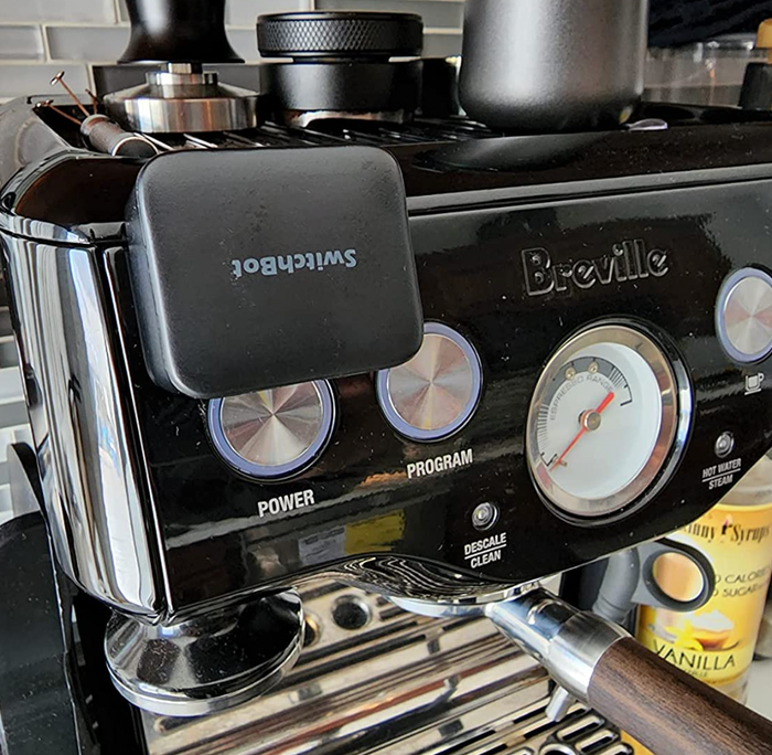 The black version of the SwitchBot Smart Switch Button Pusher mounted on a coffee machine button.