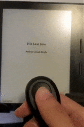 A reviewer using a compact black remote to flip through pages on a Kindle.