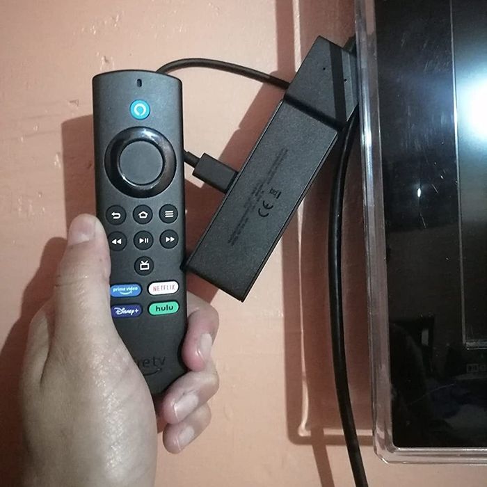 A reviewer holding the included remote up to the plugged-in Fire Stick.