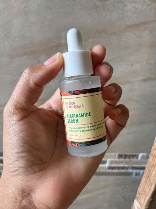 A hand holds a bottle of Good Molecules Niacinamide Serum, showcasing its claim to refine skin tone and enhance the appearance of pores.