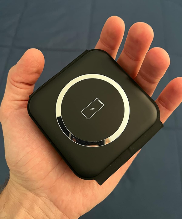 A person holding a compact, square-shaped wireless charging pad with a circular charging indicator glowing in the center.